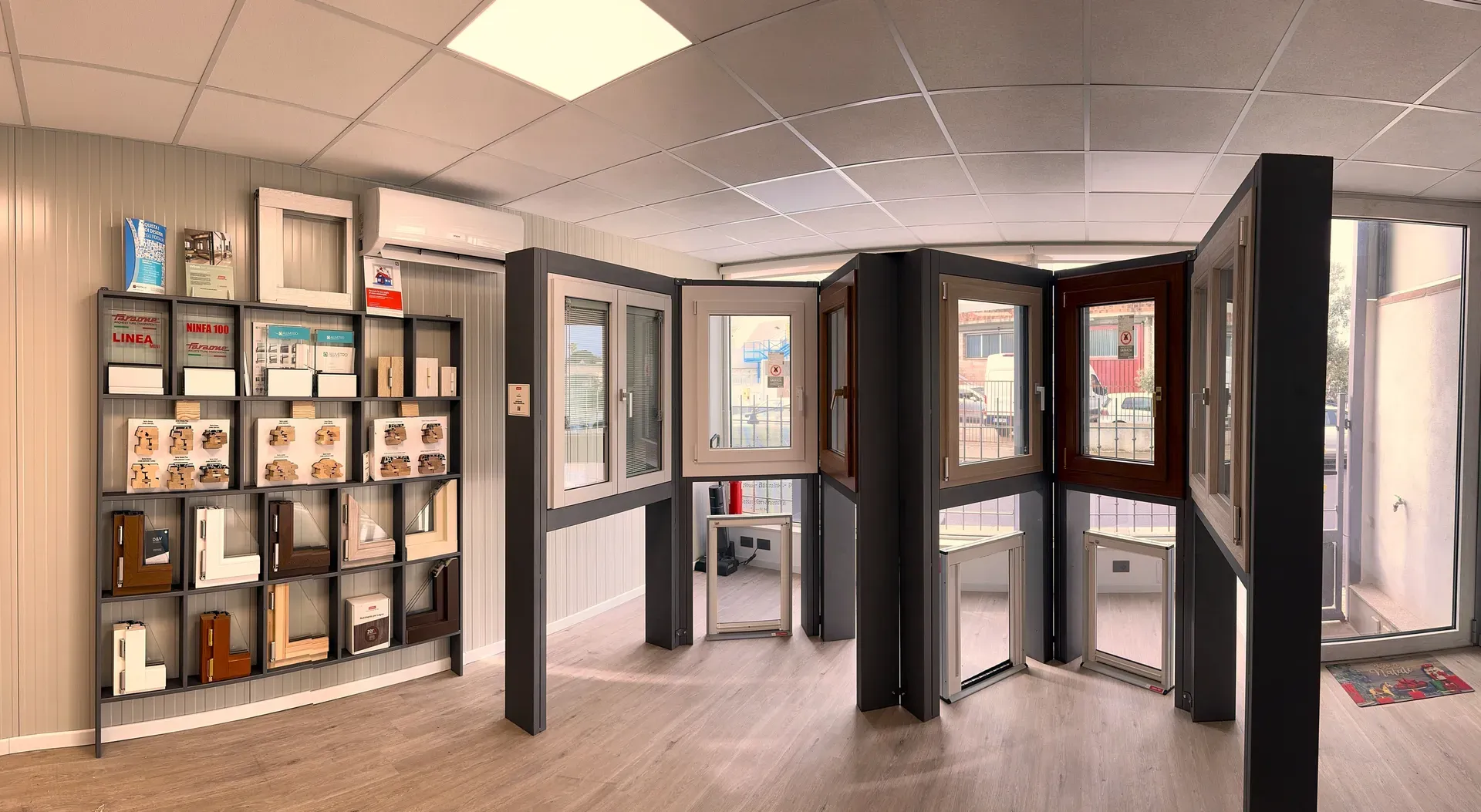 Showroom con finestre bianche e in legno su espositori grigi, scaffale di profili in sezione e cataloghi Ninfa 100